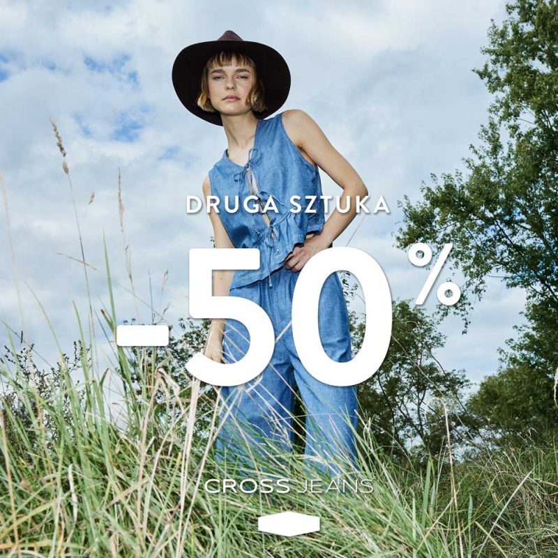 Modelka w dżinsowym komplecie marki Cross Jeans stoi na łące wśród traw; na grafice widoczna informacja o promocji „druga sztuka -50%”.