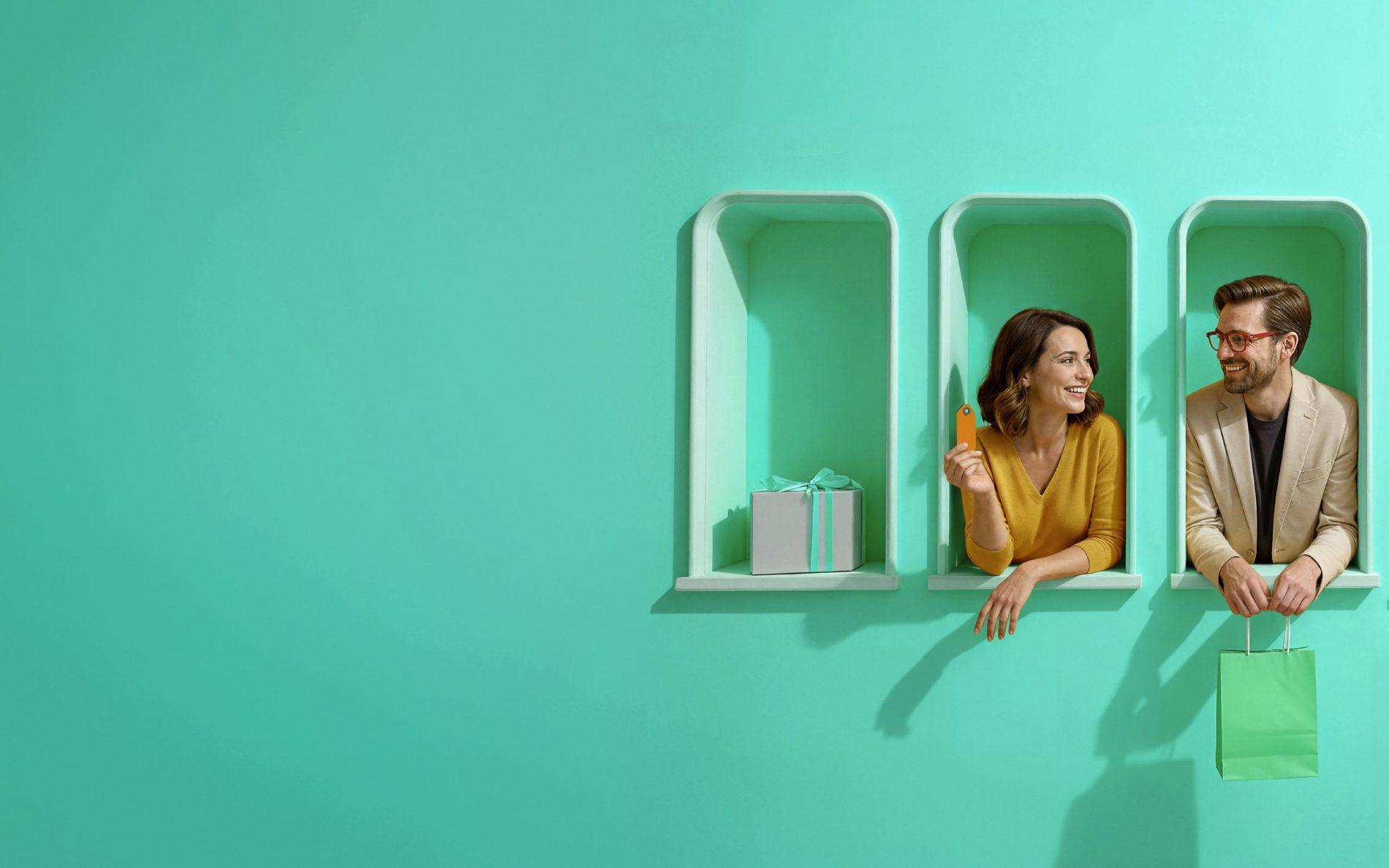 Kobieta i mężczyzna wychylają się z turkusowych wnęk w ścianie, trzymając kartę płatniczą oraz torbę zakupową; obok widoczne są pudełko prezentowe i torba na zakupy.