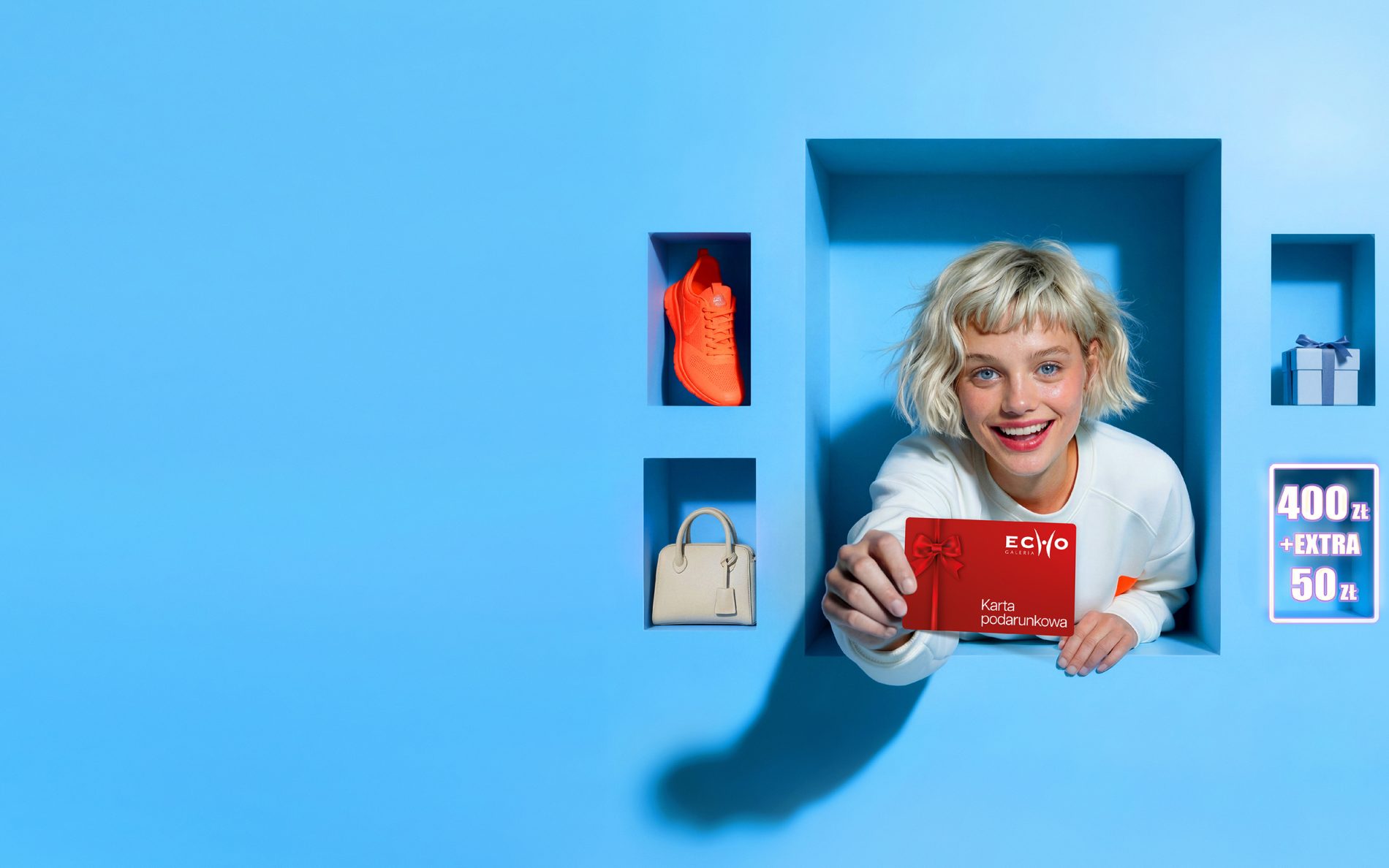 Uśmiechnięta kobieta z prezentami promująca akcję 50 zł bonusu do Karty Podarunkowej w Galerii Echo.