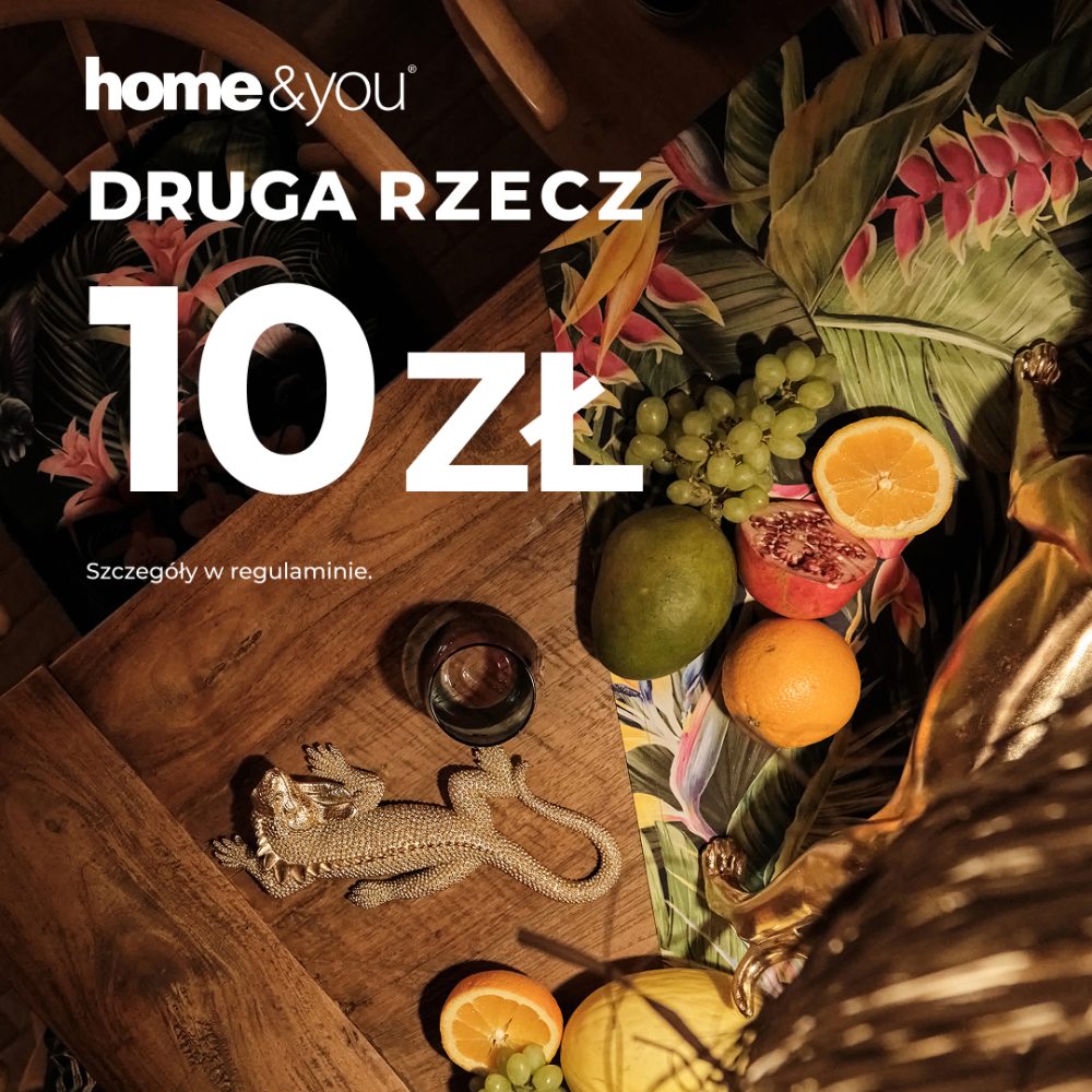 Grafika promocyjna marki home&you informująca o akcji „DRUGA RZECZ 10 ZŁ” na tle nastrojowej aranżacji wnętrza. Zdjęcie przedstawia drewniany stół z tropikalnymi dodatkami, owocami takimi jak mango, winogrona i cytrusy oraz złotą figurką jaszczurki. W górnej części kompozycji widoczne jest białe logo marki oraz wyraźny napis z ceną promocyjną.
