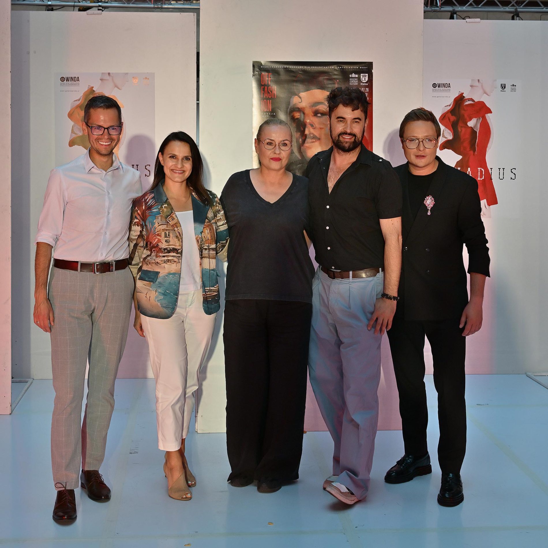 Zdjęcie przedstawia pięć uśmiechniętych osób stojących obok siebie i pozujących do zdjęcia na tle plakatów z napisem „OFF FASHION”. Grupa składa się z trzech mężczyzn i dwóch kobiet ubranych w eleganckie oraz casualowe, stylowe stroje.