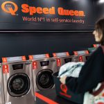 Klientka z koszem na pranie przed ciągiem profesjonalnych pralek w Speed Queen.