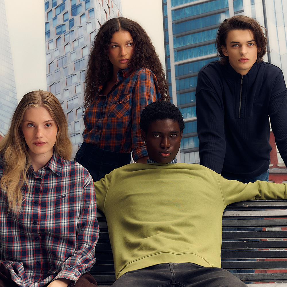 Kwadratowa fotografia wizerunkowa nowej kolekcji marki Lee Cooper. Na zdjęciu widać czwórkę młodych osób (dwie kobiety i dwóch mężczyzn) pozujących na tle wieżowca. Po lewej kobieta w koszuli w czerwoną kratę, obok kobieta w koszuli w pomarańczowo-niebieską kratę, na dole mężczyzna w oliwkowej bluzie, a po prawej mężczyzna w ciemnogranatowej bluzie zapinanej pod szyją.