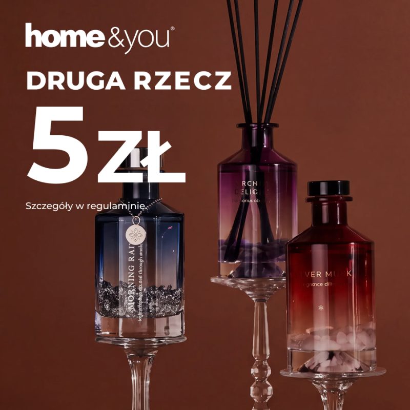 Fioletowy dyfuzor z czarnymi patyczkami między granatowym i bordowym flakonem z ozdobnymi kamieniami, na wysokich szklanych podstawkach i brązowym tle