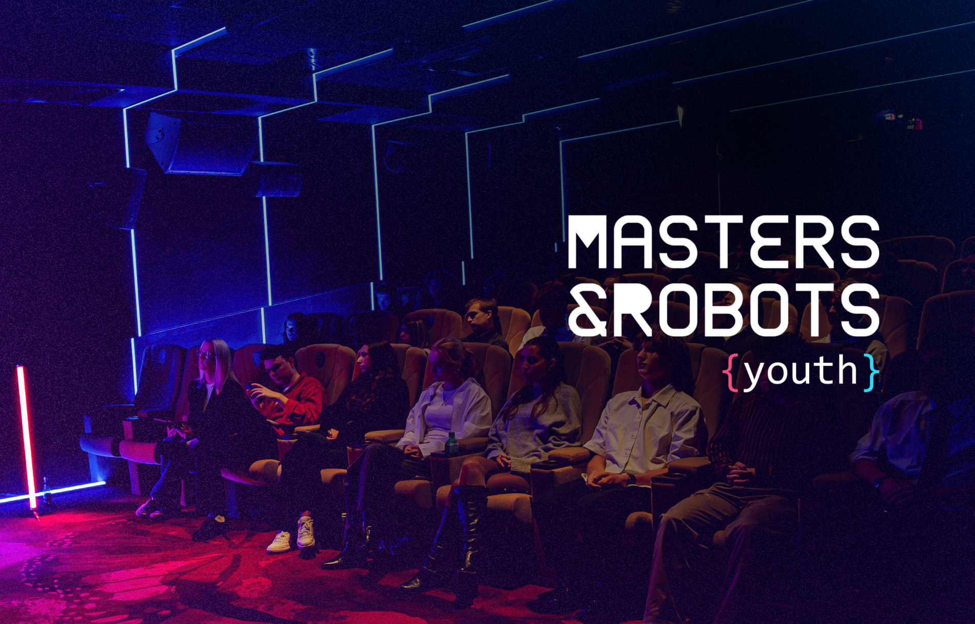 Grafika promocyjna konferencji „Masters & Robots {youth}”. Na zdjęciu widoczna jest zaciemniona sala kinowa z rzędami foteli, w których siedzą uczestnicy wydarzenia. Wnętrze oświetlone jest nastrojowym, niebieskim i czerwonym światłem. W prawej części grafiki znajduje się biały napis z tytułem konferencji „MASTERS & ROBOTS {youth}”